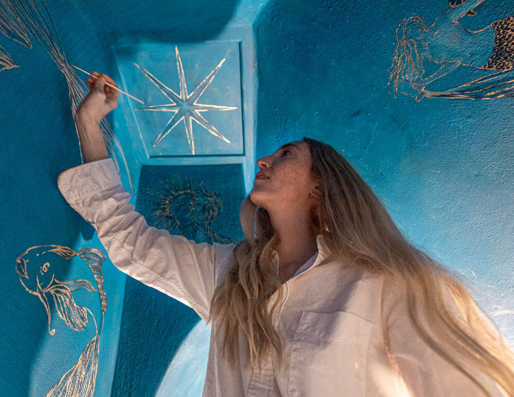 Holly Biörklund painting a celestial mural on a blue wall